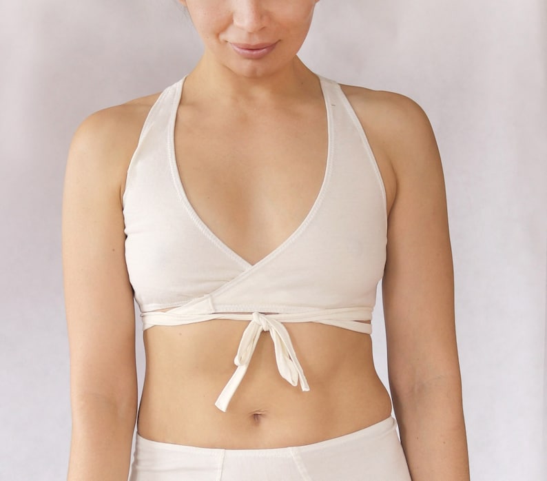 May include: A white wrap-style bralette with adjustable straps. The bralette is made of a soft, stretchy fabric and has a deep V-neckline.