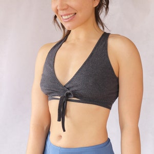 May include: A dark grey wrap-style sports bra with a tie at the front. The bra is made of a soft, stretchy fabric.