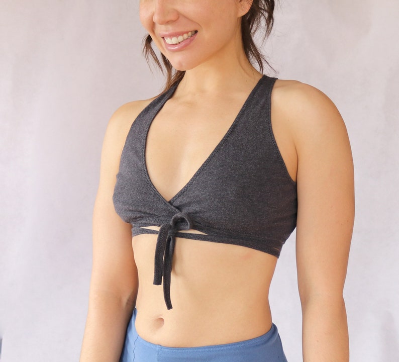 May include: A dark grey wrap-style sports bra with a tie at the front. The bra is made of a soft, stretchy fabric.