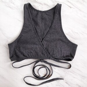 May include: A grey wrap-style top with adjustable straps. The top is made from a soft, stretchy fabric and has a relaxed fit.