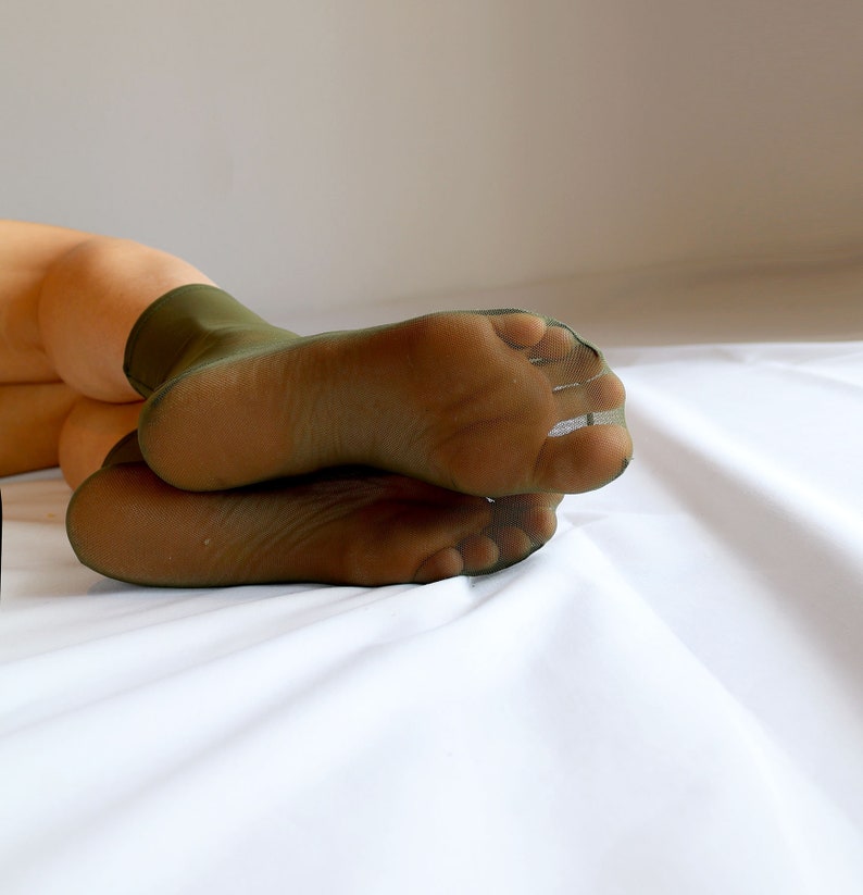 May include: A pair of green sheer socks with the toes and heels showing. The socks are lying on a white surface.