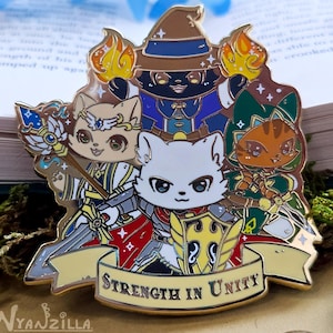 May include: Gold enamel pin featuring four cartoon cats in different roles: a wizard, a warrior, a mage, and a paladin. The cats are arranged in a circle around a banner that reads "Strength in Unity".