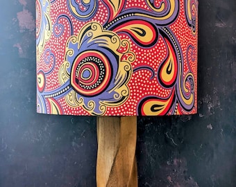 May include: A lampshade with a red, yellow, and purple paisley pattern. The lampshade is made of fabric and has a white background with small white dots.