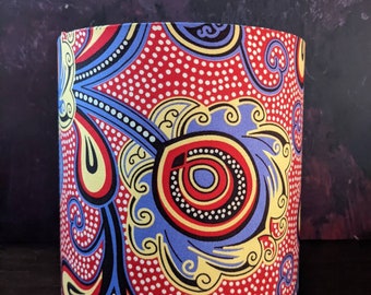 May include: A red, blue, yellow, and black patterned lampshade with a white polka dot background. The lampshade is cylindrical and has a curved top.
