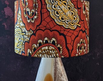 May include: A lampshade with a red, orange, and yellow floral pattern. The pattern features large, stylized flowers and leaves. The lampshade is made of fabric and has a white lining.
