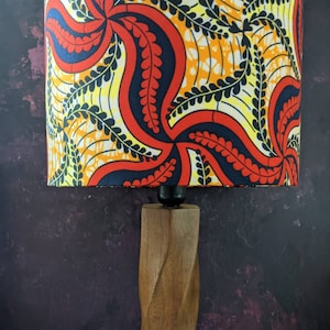 May include: A wooden table lamp with a red, yellow, and black patterned lampshade. The lampshade has a swirling design with leaves.