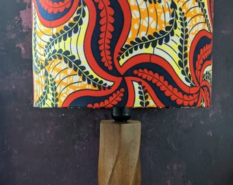 May include: A wooden table lamp with a red, yellow, and black patterned lampshade. The lampshade has a swirling design with leaves.