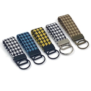 May include: Five keychains with houndstooth patterns in various colors: black and white, blue and white, yellow and black, and brown and tan. Each keychain has a metal ring and a black or silver metal clasp.