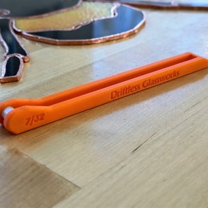 May include: Orange plastic tool with a groove for holding glass. The tool is labeled "Driftless Glassworks" and "7/32".