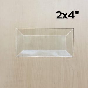 May include: A clear plastic tray with a beveled edge. The tray is 2 inches by 4 inches.