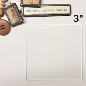 May include: A 3-inch square piece of clear glass with a white background. The glass is framed with a thin, silver-colored metal frame.