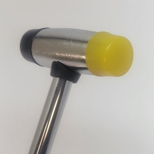 May include: A silver hammer with a yellow rubber head. The hammer has a black handle.