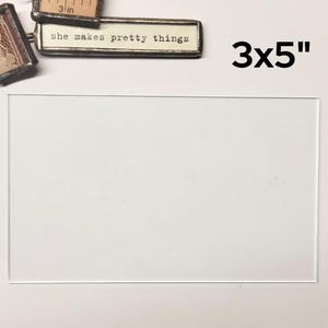 May include: A white mat with a 3x5 inch opening. The mat is surrounded by a white border.