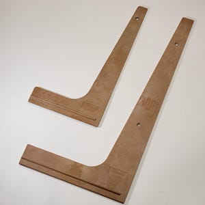 May include: Two wooden L-shaped rulers with a groove on the bottom edge. The rulers are made by the company "L-Square" and have holes drilled along the long edge.