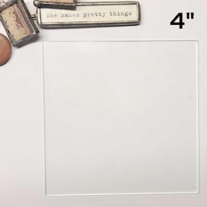 May include: A clear glass square tile measuring 4 inches by 4 inches. The tile is on a white surface.