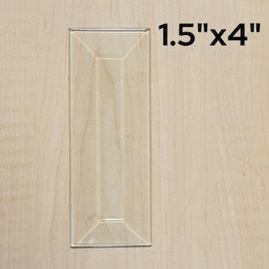 May include: A clear glass tile with a beveled edge, measuring 1.5 inches by 4 inches.
