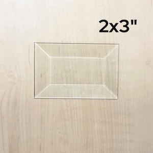 May include: A clear acrylic picture frame with a 2x3 inch opening. The frame is made of a thick, durable acrylic and has a smooth, polished finish.