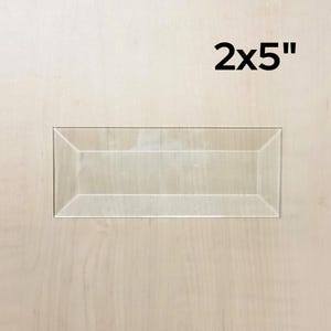 May include: A clear acrylic rectangular tray with beveled edges. The tray measures 2 inches by 5 inches.