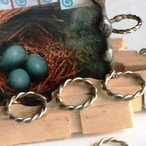 May include: Close-up of four silver, twisted wire rings. The rings are arranged in a row on a wooden surface. The rings are all the same size and have a smooth, polished finish.