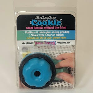 Puede incluir: Una herramienta Grinder Cookie azul y negra en un embalaje de plástico transparente. El embalaje incluye el texto "Great Results without the Grind" y "Positions & holds glass during grinding". La herramienta está diseñada para prolongar la vida útil de un cabezal de amoladora.