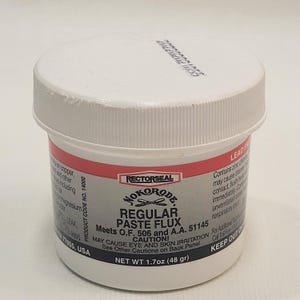 May include: A white plastic jar with a red label that reads "NOKORODE REGULAR PASTE FLUX" and "Meets O.F. 506 and A.A. 51145". The label also includes a warning that the product may cause eye and skin irritation. The jar contains 1.7 ounces (48 grams) of flux.