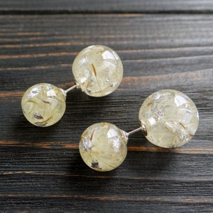 May include: A pair of silver post earrings with two round, clear resin beads. Each bead is filled with dried flowers and silver flakes.