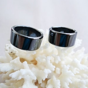 May include: Two black hematite rings on a white coral background. The rings are smooth and shiny.