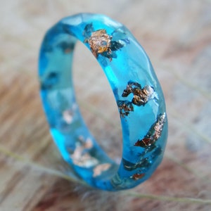 May include: A turquoise blue resin ring with gold flecks embedded in the resin.