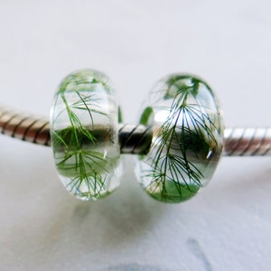 May include: Two clear glass beads with green plant material inside, on a silver chain bracelet.