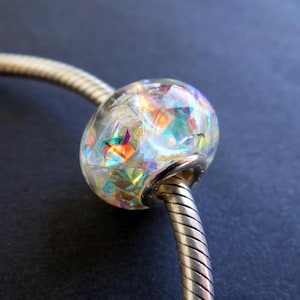 May include: A silver charm bracelet with a clear iridescent glass bead. The bead is filled with small, colorful pieces of glass that create a shimmering effect.