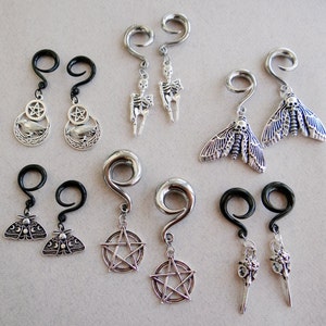 May include: A set of eight silver and black dangle earrings with various charms, including a skull, a moth, a pentagram, and a crow. The earrings are designed for stretched earlobes.