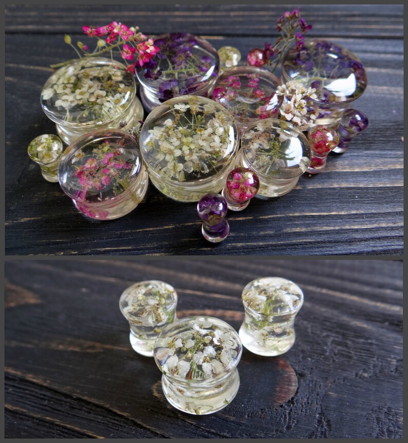 May include: Assortment of clear resin ear gauges with embedded dried flowers. The gauges are various sizes and feature different flower arrangements, including white, pink, and purple flowers.