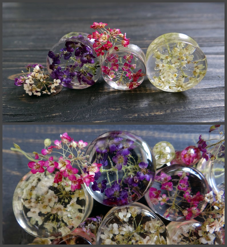 May include: Assortment of clear resin ear gauges with pressed flowers. The gauges feature purple, pink, and white flowers.