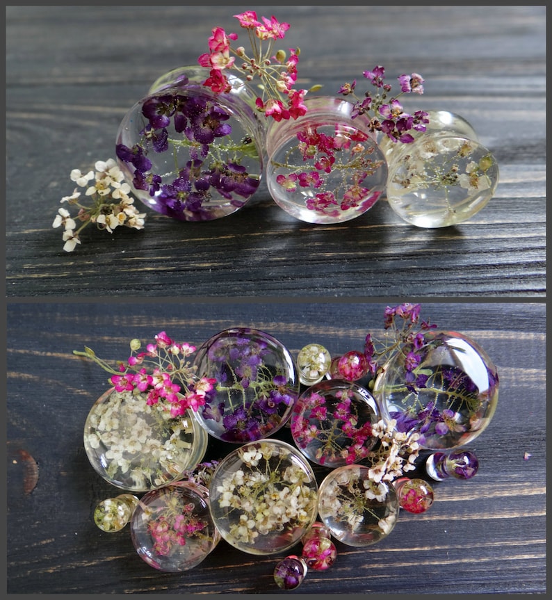 May include: Assortment of clear resin ear gauges with pressed flowers and leaves. The gauges feature a variety of colors, including white, pink, purple, and green.