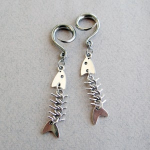 May include: A pair of silver fishbone earrings with a spiral design. The earrings are made of metal and have a silver finish.