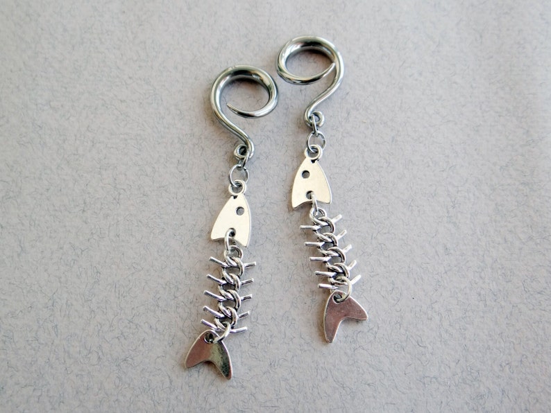 May include: A pair of silver fishbone earrings with a spiral design. The earrings are made of metal and have a silver finish.