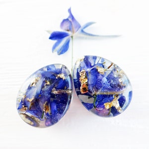 May include: Two clear resin earrings with blue flower petals and gold flakes inside.