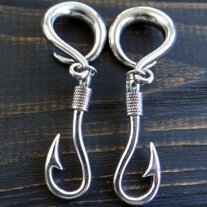 Op de afbeelding: Een paar zilveren metalen oorpluggen met een vishaakontwerp. De pluggen zijn rond en hebben een gladde afwerking.