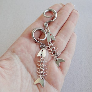 May include: A pair of silver fishbone earrings with a curved hook. The earrings are made of metal and have a detailed fishbone design.