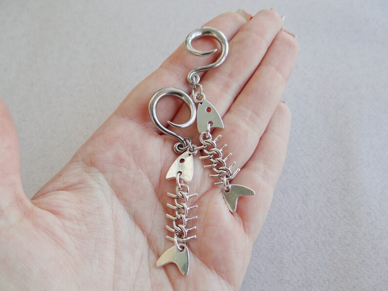 May include: A pair of silver fishbone earrings with a curved hook. The earrings are made of metal and have a detailed fishbone design.