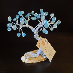May include: A white wire tree with blue glass beads, a wooden base, and a thank you tag that reads "Thank you for celebrating with us! Jeremiah's Baby Shower August 8, 2021"