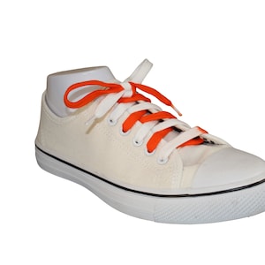 Puede incluir: Zapatilla de lona color crema con puntera y suela de goma blanca. Cordones naranjas y blancos, una franja negra en la suela y diseño de corte bajo. La zapatilla se muestra sobre un fondo blanco.