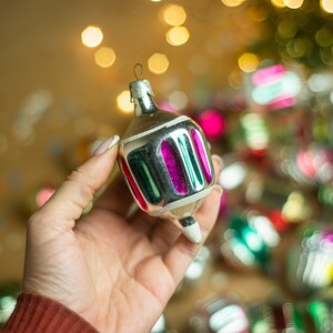 May include: A silver Christmas ornament with green and pink stripes. The ornament is shaped like a spinning top and has a pointed tip.