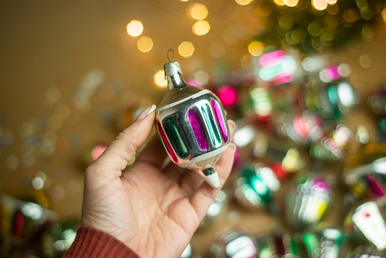 May include: A silver Christmas ornament with green and pink stripes. The ornament is shaped like a spinning top and has a pointed tip.