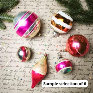 Puede incluir: Un conjunto de seis adornos navide&ntilde;os de cristal de diversas formas y tama&ntilde;os. El set incluye bolas esf&eacute;ricas y con forma de l&aacute;grima con acabados met&aacute;licos en rosa, dorado y plateado, decoradas con rayas horizontales o espirales blancas.