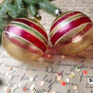 Puede incluir: Dos adornos navide&ntilde;os de vidrio redondos con acabado dorado met&aacute;lico y bandas horizontales de rayas rojas y verdes. Cada adorno tiene una tapa de metal plateado en la parte superior. El texto SET 6 es visible en la esquina inferior derecha.