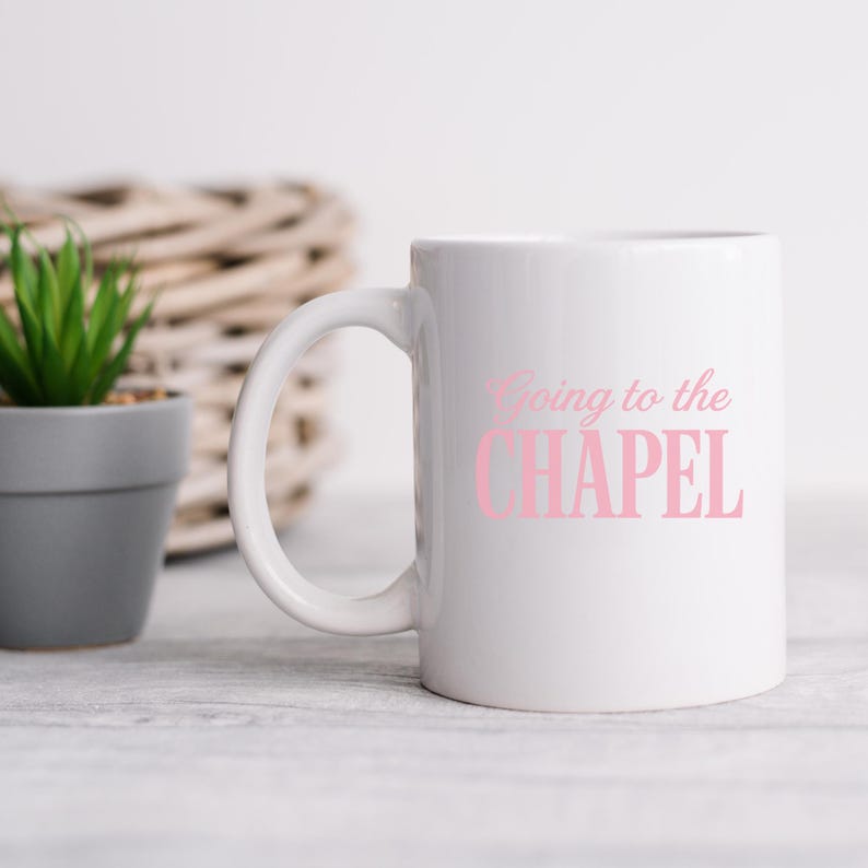 Puede incluir: Una taza de cer&aacute;mica blanca con el texto Going to the CHAPEL impreso en una fuente de color rosa claro que combina estilo cursivo y letras de bloque. La taza tiene un acabado liso y un asa curva en el lado izquierdo para facilitar su agarre.