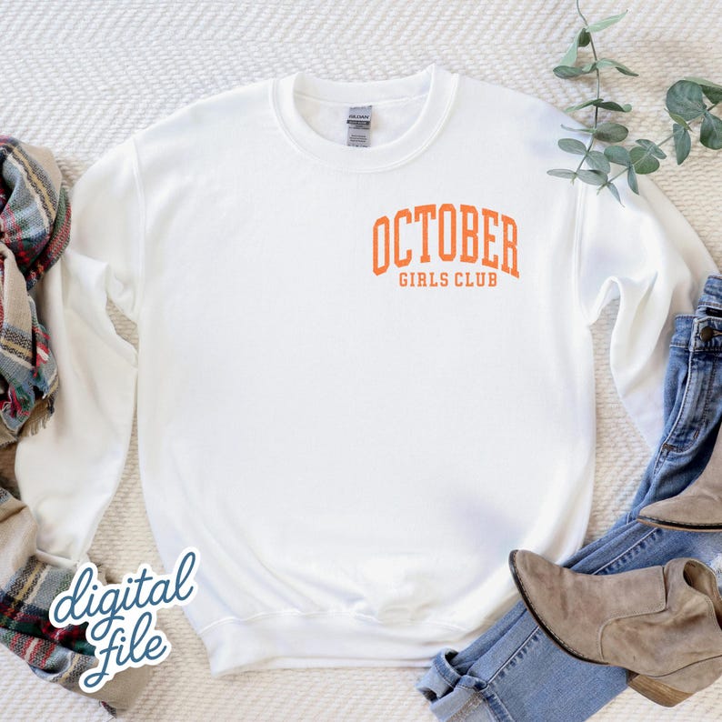 May include: A white long-sleeve crewneck sweatshirt featuring the orange text OCTOBER GIRLS CLUB printed in a collegiate font on the upper left chest area. The garment has a ribbed collar, cuffs, and hem, and is displayed on a textured surface.