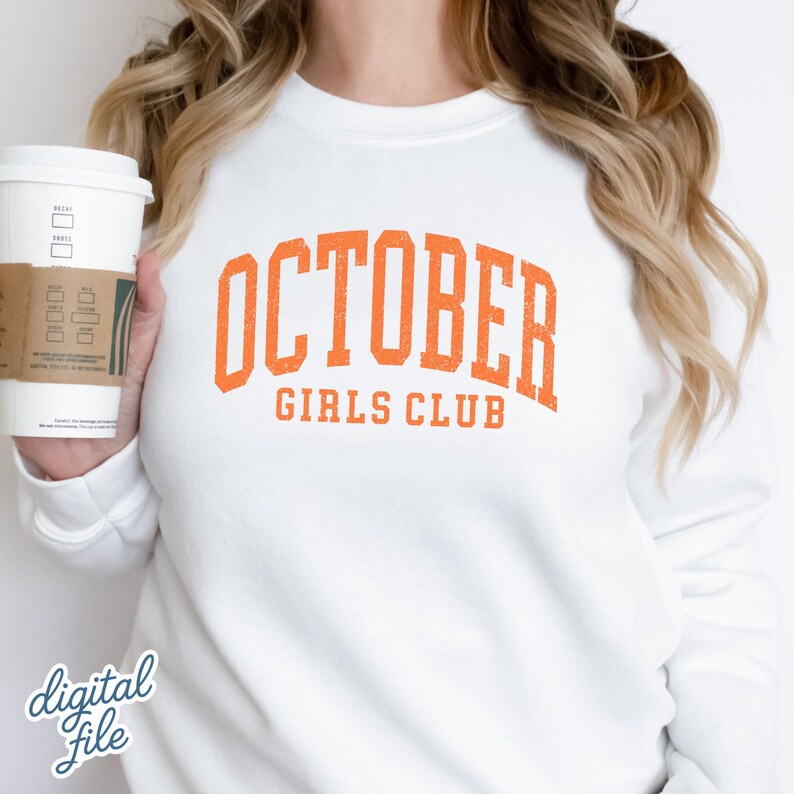 May include: A white crewneck sweatshirt featuring the orange text OCTOBER GIRLS CLUB in a distressed collegiate font across the chest. The garment is shown in a plain white color with long sleeves and a ribbed neckline, presented as a clean design.