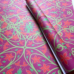 May include: Purple wrapping paper with a repeating pattern of green vines and red flowers. The paper is rolled up and the end is visible.
